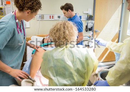 Woman having contraction giving birth in hospital with medical team ready.