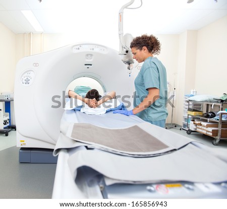 Female patient undergoing CT scan test while nurse looking at her in examination room