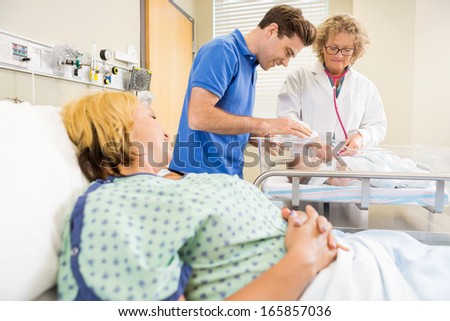 Female mature doctor examining newborn baby while parents looking at her in hospital