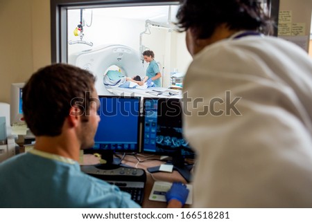 Radiologist and nurse operating computers while nurse preparing patient for CT scan in hospital