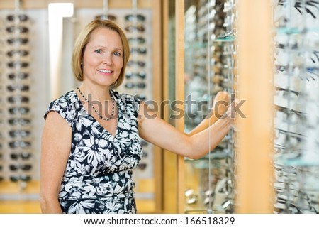 Portrait of happy female customer selecting glasses in optician store
