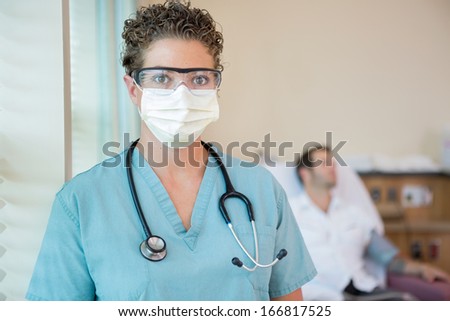 Portrait of female nurse in protective clothing with patient in background at hospital room
