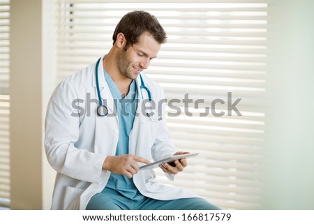 Young male cancer specialist in labcoat using digital tablet at clinic