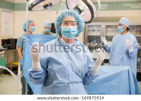 Mature female doctor in surgical gown with team standing at operation room