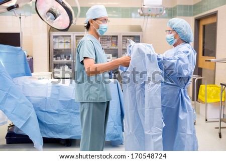 Scrub nurse assisting surgeon with sterile gown in surgical theater