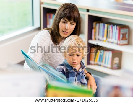 Elementary student with teacher reading book in school library