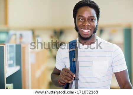 Happy male student carrying backpack while looking away in bookstore