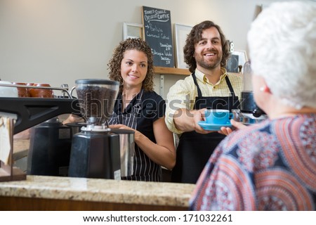 Smiling cafe owners serving coffee to senior woman at counter