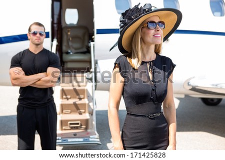 Happy woman wearing sunhat and sunglasses with bodyguard and private jet in background