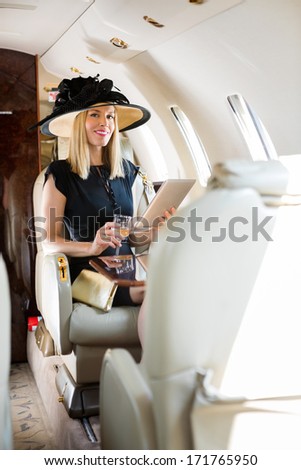 Portrait of rich confident woman with digital tablet and drink glass sitting in private jet