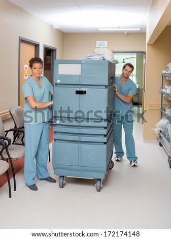 Full length of nurses pushing trolley in hospital hallway