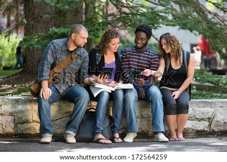 Multiethnic university students using digital tablet while studying on parapet at campus