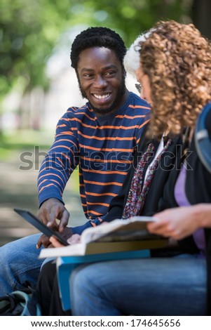 Happy male university student using digital tablet with female friends on campus