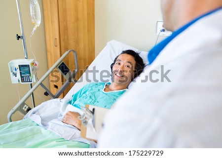 Happy mature male patient looking at doctor while lying on bed in hospital