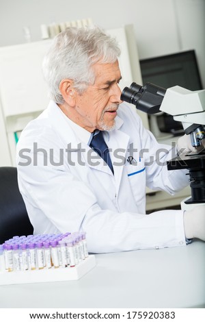 Senior male healthcare worker looking into microscope in laboratory