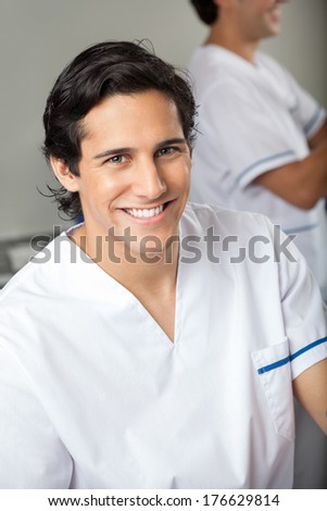 Portrait of happy male technician in medical laboratory with colleague in background