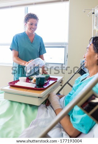 Mid adult nurse lifting cover from food plate for male patient in hospital