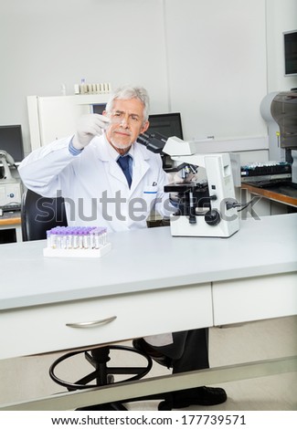 Senior male researcher analyzing microscope slide in medical lab