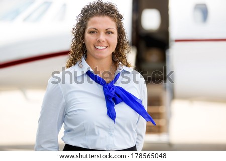 Portrait of beautiful airhostess with private jet in background at terminal