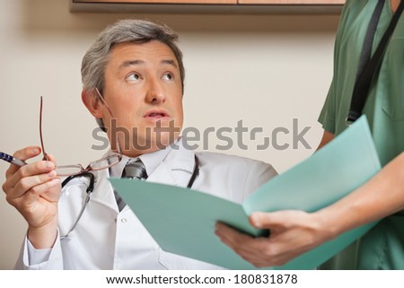 Mature male doctor staring while technician holding patient\'s file