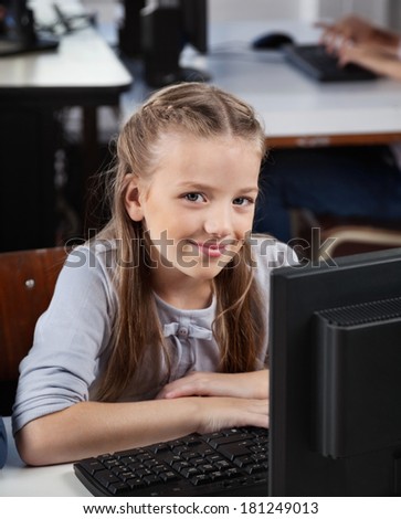 Portrait of cute schoolgirl sitting with computer at desk in lab
