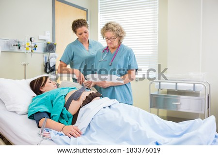 Female Nurses inspecting fetal monitor report with expecting mother looking on