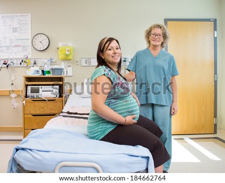 Portrait of happy mature female nurse and pregnant woman in hospital room