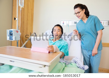 Mature male patient using digital tablet while nurse pointing at it in hospital