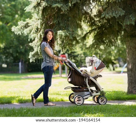 Full length portrait of young mother pushing stroller in the park