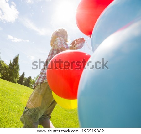 Young boy with helium balloons walking in green meadow