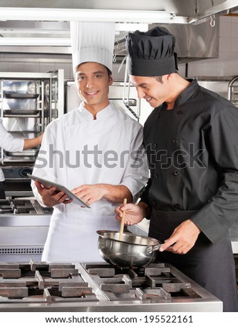 Male chefs with digital computer cooking food in commercial kitchen