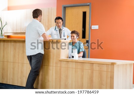 Doctor and nurse working at reception desk while patient standing in hospital