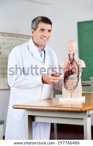 Happy mature male professor looking away while analyzing anatomical model in classroom