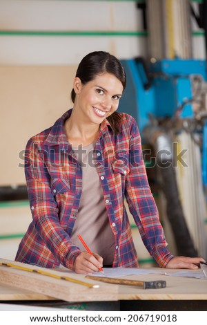 Portrait of happy female carpenter writing on paper in workshop