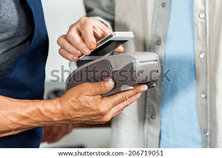 Midsection of salesman accepting payment through NFC technology from customer in hardware store