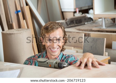 Happy mid adult carpenter drilling wood in workshop