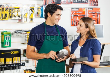 Happy woman with tool set looking at worker swiping credit card in hardware store