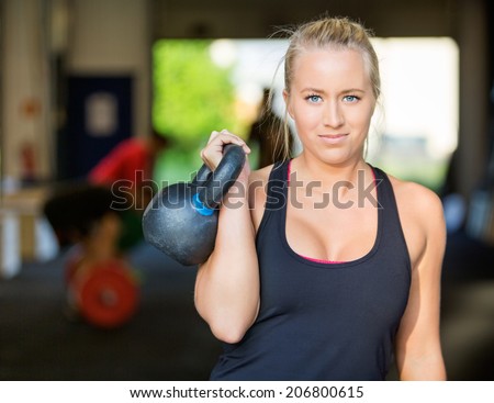 Portrait of confident female athlete lifting kettlebell at gym