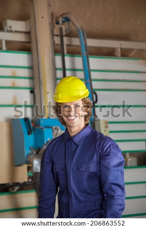 Portrait of confident carpenter standing against vertical saw machine in workshop
