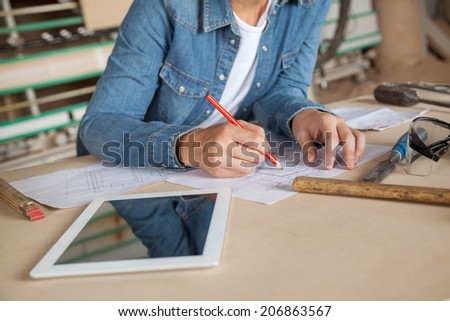 Midsection of female carpenter drawing on blueprint at table in workshop