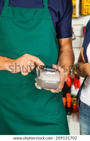 Midsection of male worker accepting payment through smartphone in store