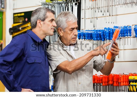 Senior male customer examining packed screwdriver while vendor looking at it in hardware shop