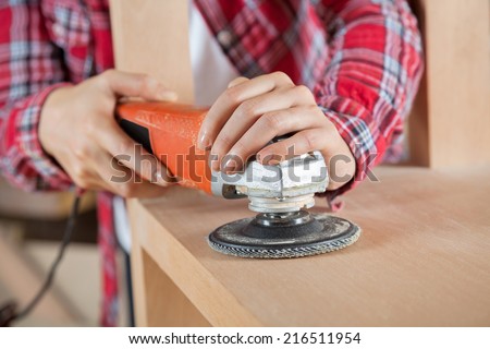 Female carpenter\'s hands using sander on wooden shelf in workshop