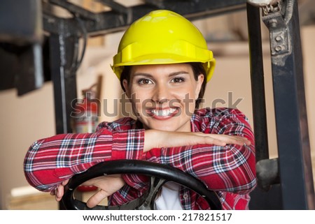 Portrait of happy engineer wearing hardhat while leaning on steering wheel of forklift in workshop