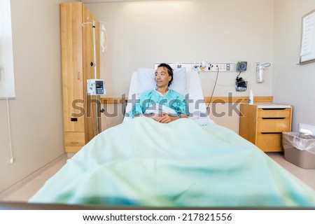 Full length of thoughtful mature male patient reclining on bed in hospital