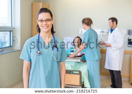 Portrait of confident nurse smiling with patient and medical team in background at hospital