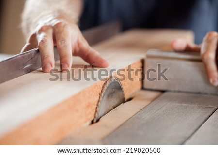Carpenter\'s hands cutting wood with tablesaw in workshop