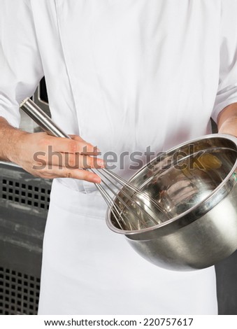 Midsection of male chef with wire whisk and mixing bowl