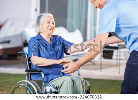 Midsection of male caretaker helping senior woman to get up from wheelchair at nursing home lawn