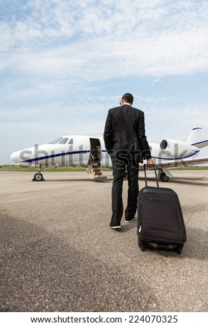 Full length rear view of businessman with luggage walking towards private jet